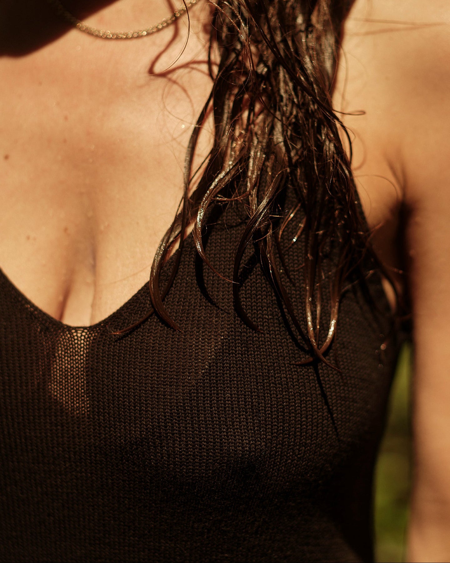 close-up of person's chest and shoulders wearing the knit mini dress outdoors in warm sunlight, with wet dark hair and a blurred green background.